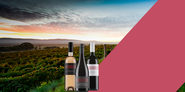 Three wine bottles in front of a scenic vineyard with a sunset.